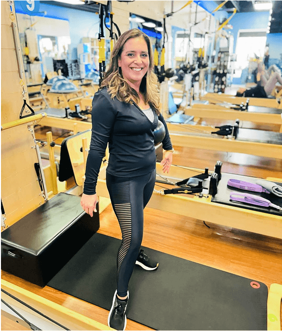 Woman in Pilates reformer room wearing black athletic wear